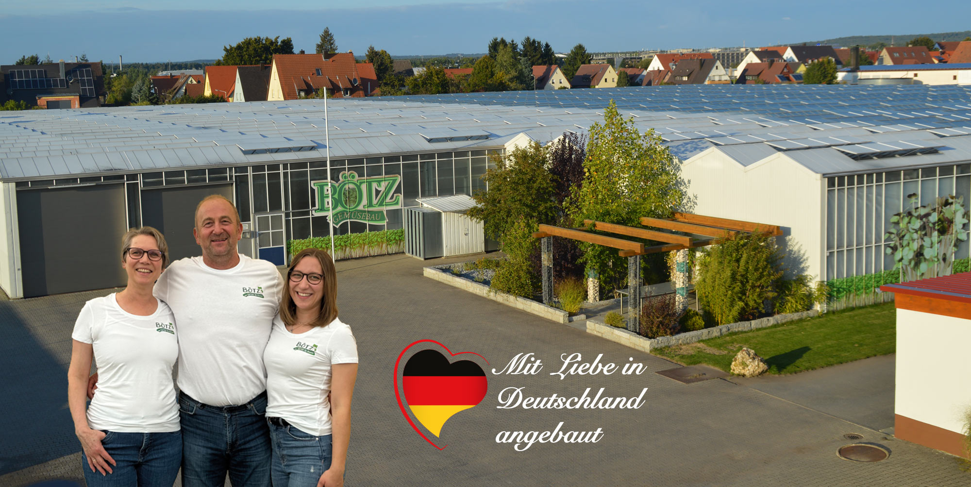 Familie Bötz (links Ehefrau Petra Bötz, rechts die Tochter Kristina, in der Mitte Roland Bötz) steht vor dem Firmengebäude, einem Glasgewächshaus mit kleiner Parkanlage vor dem Gebäude. Im Bild das Siegel der Familie, ein schwarz-rot-goldenes Herz mit dem Claim "Mit Liebe in Deutschland angebaut".